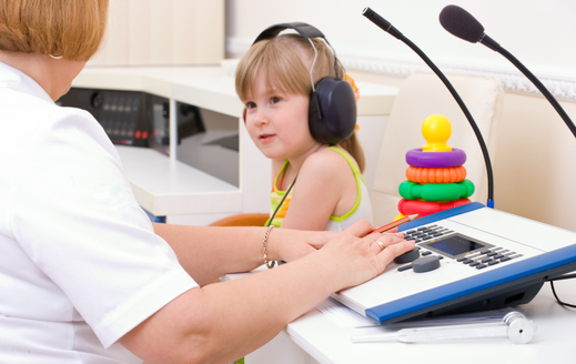 Una enfermera hace un diagnóstico de audición de una niña con cascos grandes